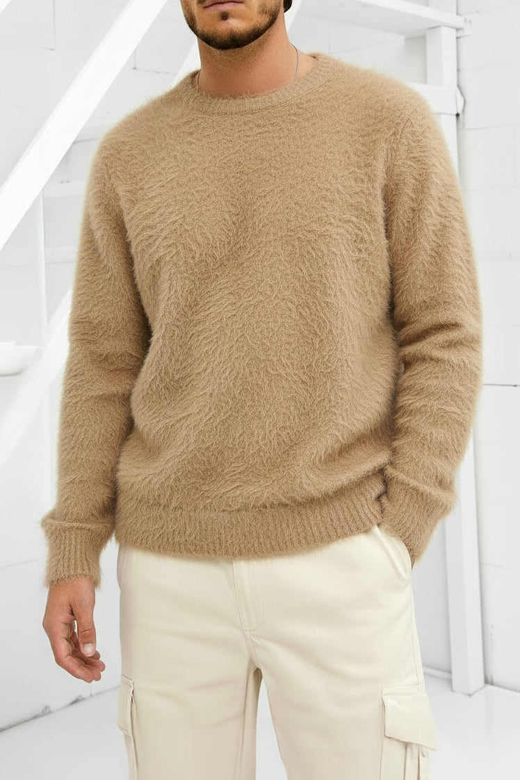 Man wearing a beige sweater and white pants in a minimalistic setting